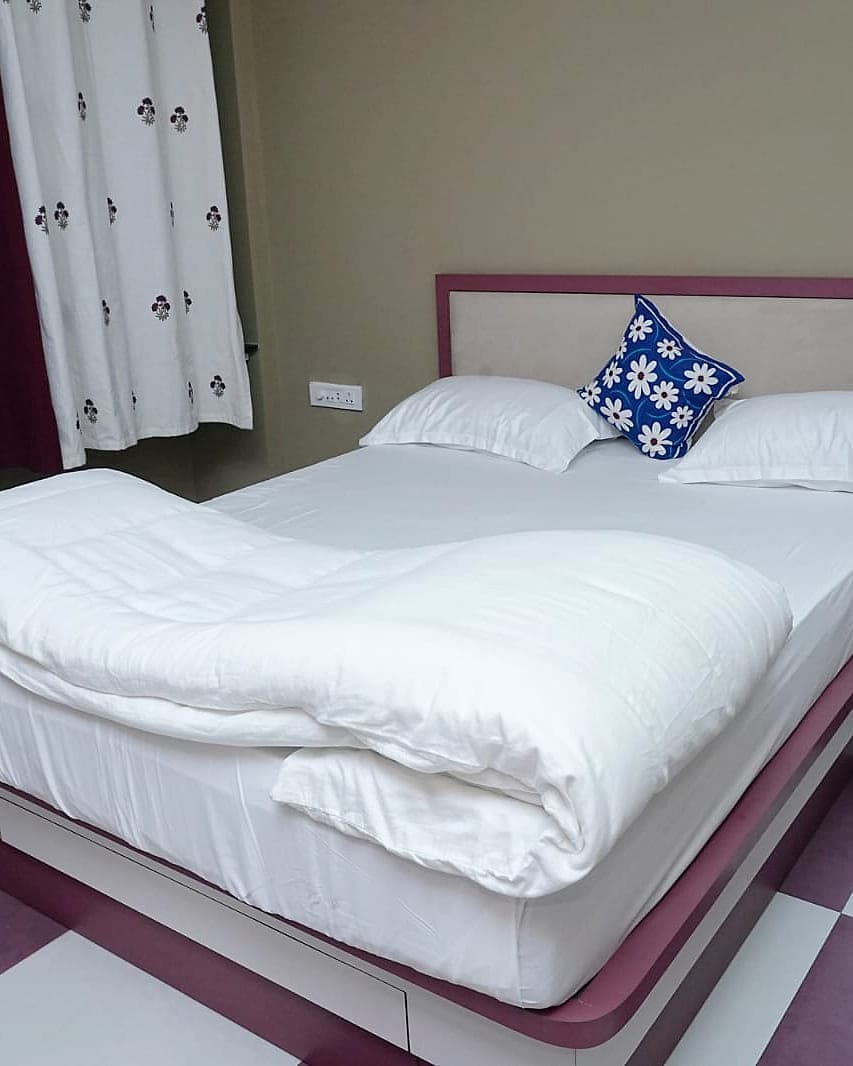 A bedroom made up in white, on a floor of maroon and white tiles.