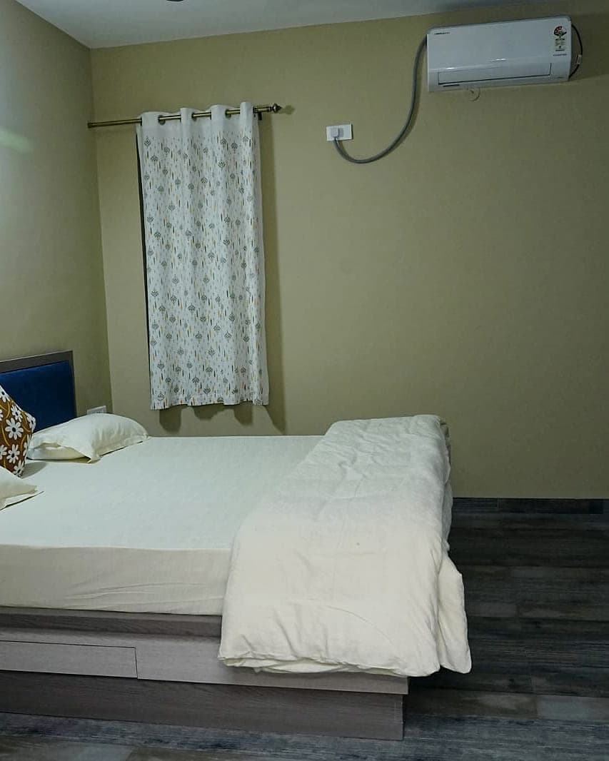A quiet bedroom with a dark headboard, a wooden floor and light curtains.