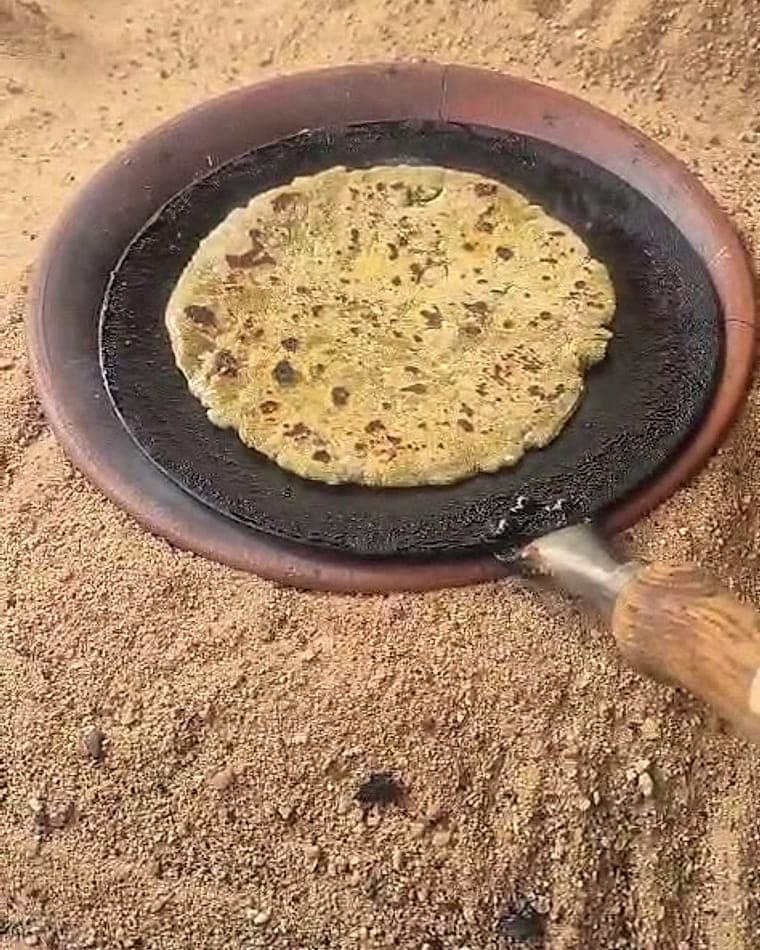 A flatbread cooking on a clay griddle over a low fire.