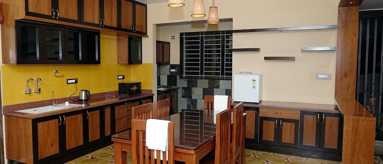 A kitchen and dining table under woven pendant shades, on a floor of patterned tiles.