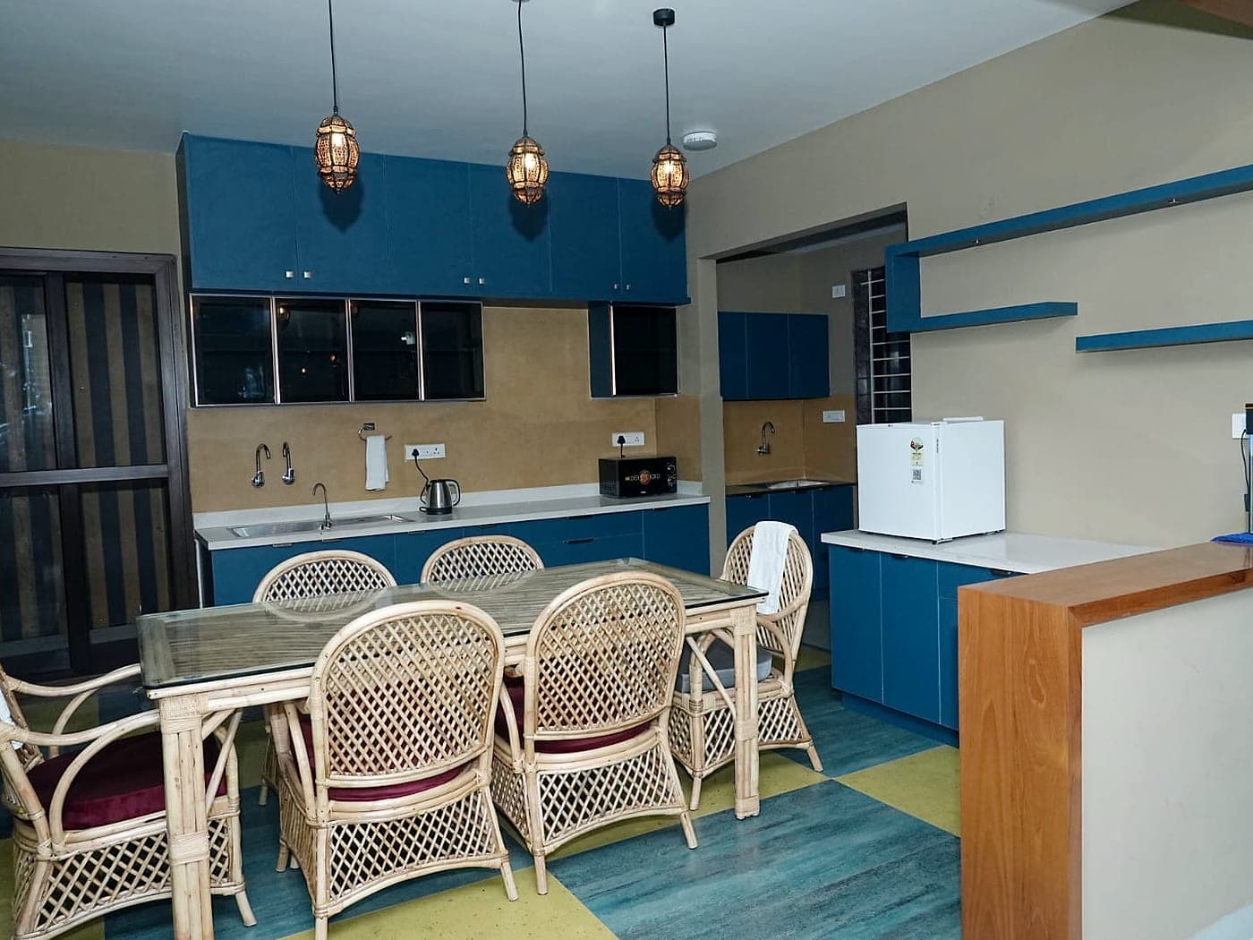 A kitchen counter with a kettle, a microwave and a small fridge beside a dining table.