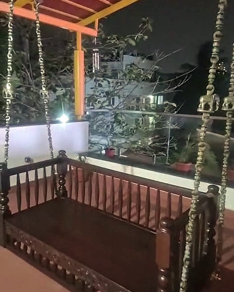 A carved wooden swing hanging on brass chains on the terrace at night, with the city beyond.