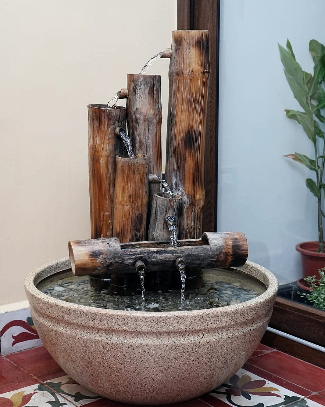 A bamboo water feature standing in a stone bowl on a patterned tiled floor.
